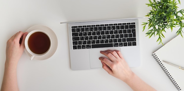 Arbeitsbereich mit der Hand des Mädchens auf Laptoptastatur und Teenotizbüchern