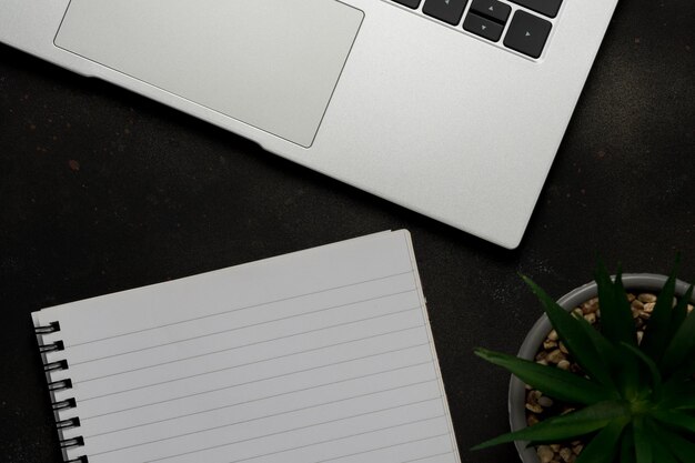 Arbeitsbereich mit leerem Notizbuch und Laptop auf schwarzem Hintergrund Draufsicht mit Kopierbereich