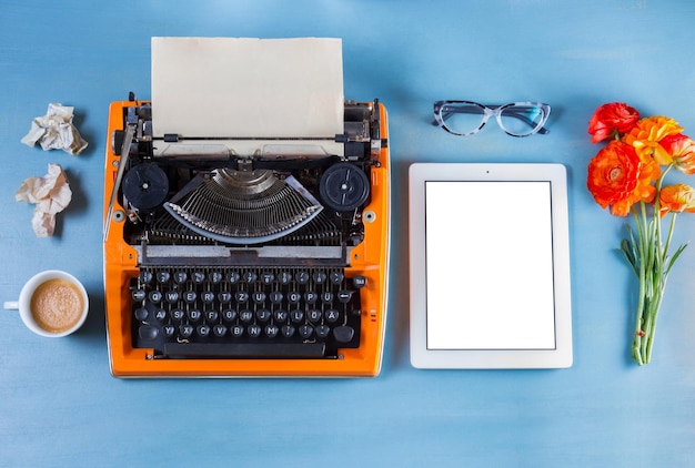 Arbeitsbereich mit orangefarbener Vintage-Schreibmaschine auf blauem Hintergrund