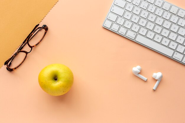 Arbeitsbereich mit Tastatur, Brille, Apfel und Ohrpolstern