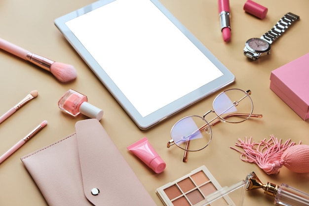 Arbeitsbereich mit weißer Tablette, Notizblock, Brille, Stiften, Schönheitszubehör auf pastellbeiger Oberfläche