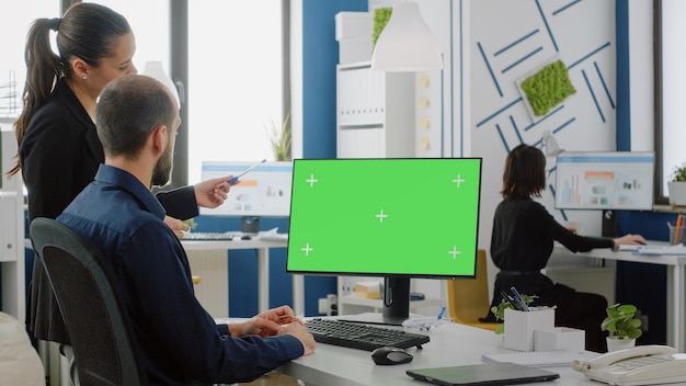 Arbeitskollegen, die Schreibtisch mit grünem Bildschirm auf Monitor für Geschäftsprojekt betrachten. Kollegen diskutieren Marketingplan und -strategie, während sie Computer mit Chroma-Key und Mockup-Vorlage verwenden