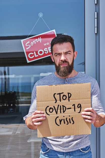 Arbeitsloser mit Schild STOP COVID19 KRISE in der Nähe von Büro oder Café mit geschlossener Tür