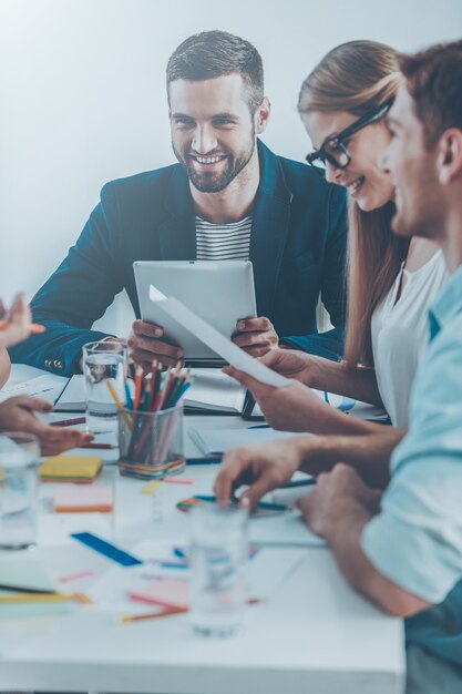 Arbeitsmomente. Gruppe von Geschäftsleuten in eleganter Freizeitkleidung, die zusammen am Tisch sitzen und lächeln