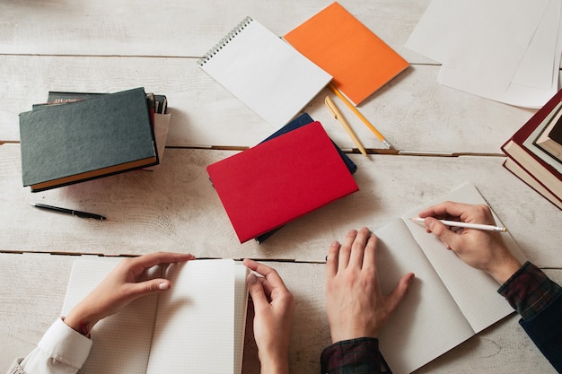 Arbeitsplatz für das Studium von Schülern mit Vorräten. Draufsicht auf Schreibtisch mit Notizbüchern und Studentenhänden, die darin schreiben.