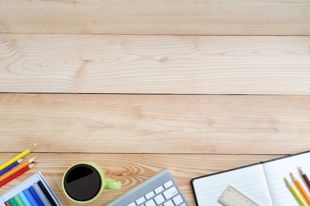 Arbeitsplatz mit Computer, Farbbleistiftnotizbuch und Kaffeetasse auf hölzernem Schreibtisch.