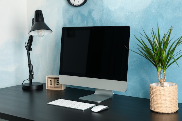 Arbeitsplatz mit Computer und Pflanze auf Holztisch. Blau und weiß