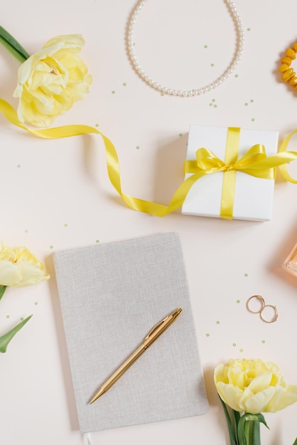 Arbeitsplatz mit einem Notizbuch und einem Stift, gelbe Tulpen, ein Armband, eine Damenhandtasche, Eau de Toilette