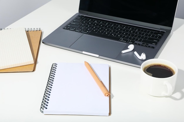 Arbeitsplatz mit Laptop und leerem Notizbuch auf weißem Tisch