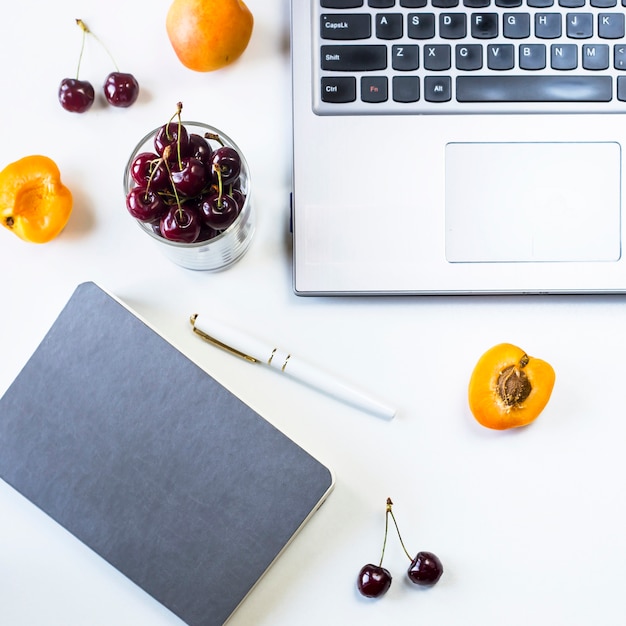 Arbeitsplatz mit Laptop und Notizblock auf weißer Tabelle mit Beeren und Fruchtsnack