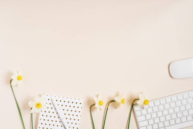 Arbeitsplatz mit Tagebuchstift-Tastaturmaus und Narzissenblumen auf hellem Hintergrund