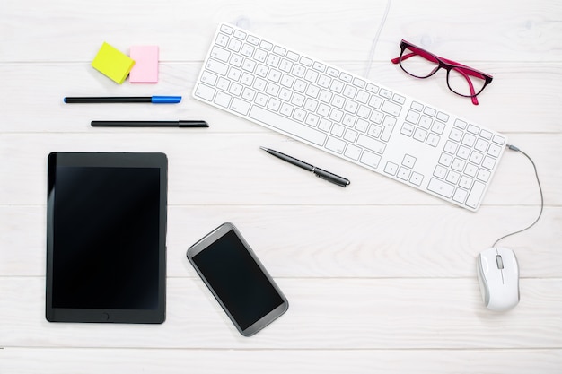 Arbeitsplatz mit Tastatur, Smartphone, Tablette und Büroartikel auf Weiß
