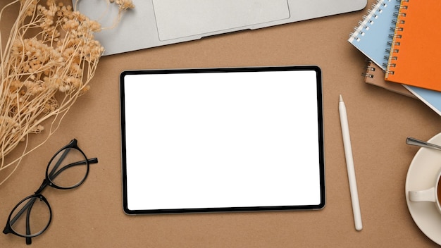 Arbeitsplatz mit weißem Bildschirmmodellbriefpapier und -brillen der Tablette auf Draufsicht des braunen Hintergrundes Beschneidungspfad eingeschlossen
