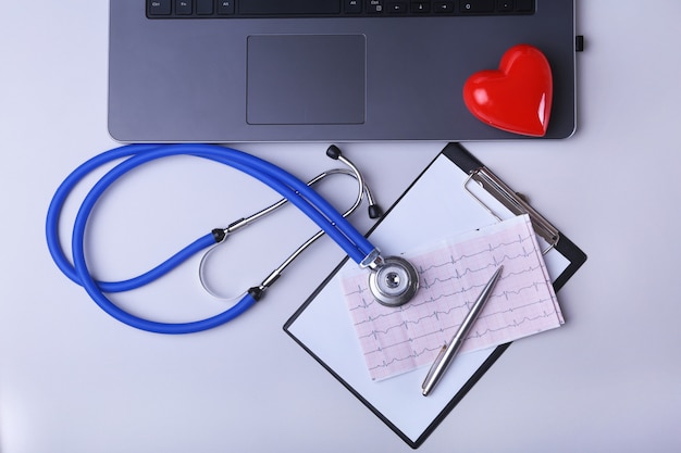 Arbeitsplatz von Doktor mit Laptop, Stethoskop, RX-Verordnung, Gläsern und rotem Herzen und Notizbuch auf weißer Tabelle. Ansicht von oben. Kopieren Sie Platz.