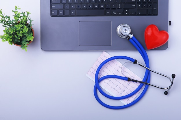 Arbeitsplatz von Doktor mit Laptop, Stethoskop, RX-Verordnung und rotem Herzen und Notizbuch auf weißer Tabelle.