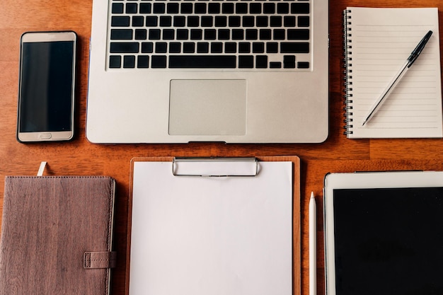 Arbeitsplatz von oben mit Laptop, Tablet, Notizblock, Papierkram, Tafel, Stift und Smartphone auf den Holztischen, Geschäft, Arbeit und Arbeitsplatz