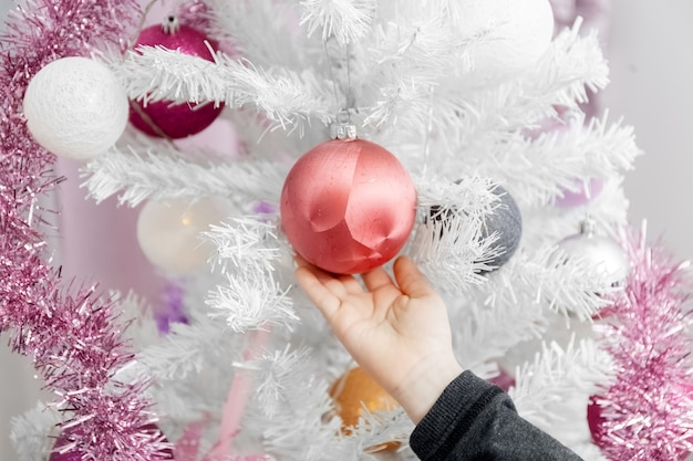 Foto Árbol de navidad blanco la mano del niño toca bolas en el árbol de navidad primer plano