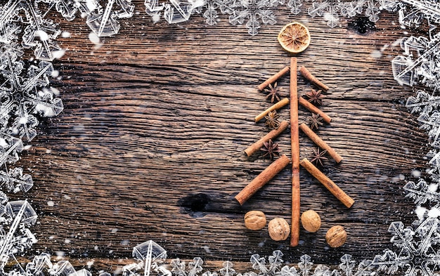 Foto Árbol de navidad de canela, anís estrellado y nueces sobre mesa de madera rustich. marco abstracto cubierto de nieve.