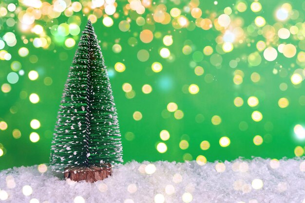 Foto Árbol de navidad cubierto de nieve sobre nieve y fondo verde con tarjeta conceptual de estandarte de navidad bokeh