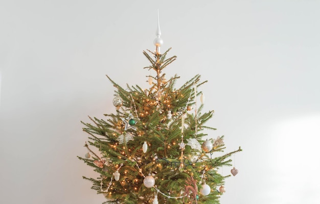 Árbol de navidad con decoración y luces en sala blanca.