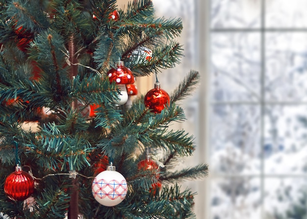 Árbol de Navidad con decoración navideña cerca de ventana congelada de invierno