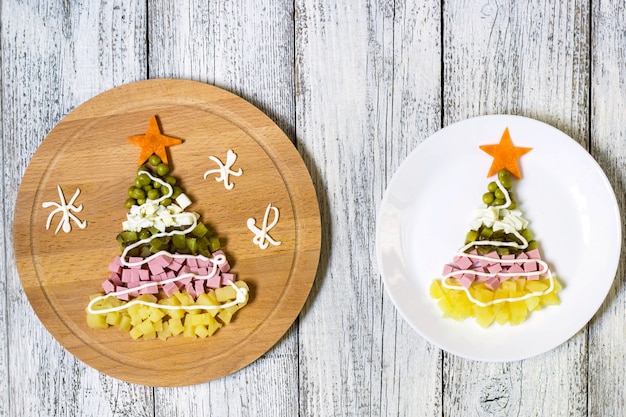 Árbol de navidad de una ensalada más olivier en placa sobre una mesa de madera blanca. vista superior con un espacio de copia