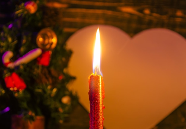 Un árbol de Navidad está detrás de una vela que se enciende con una llama roja.