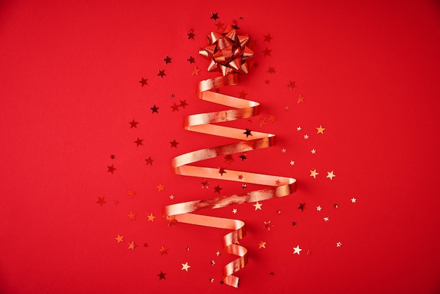 Árbol de Navidad hecho de cinta festiva y confeti sobre fondo rojo. Decoración navideña