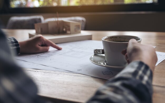 Architekt, der an einem Architekturmodell mit Geschäftszeichenpapier beim Trinken des Kaffees arbeitet