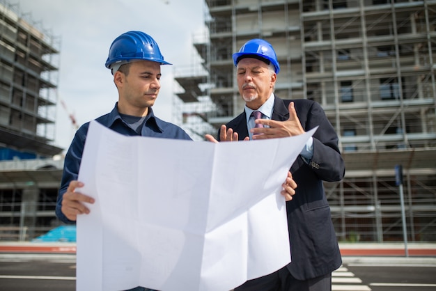 Architekt im Gespräch mit dem Bauleiter vor einem Baustellengebäude