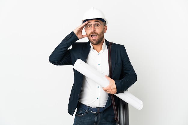 Architekt Mann mit Helm und hält Blaupausen lokalisiert auf weißer Wand mit Überraschungsausdruck
