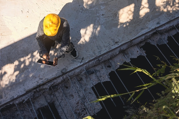 Architekt oder Bauingenieur mit Bauarbeiterhelm auf der Baustelle, der den Zeitplan auf dem Tablet-Computer überprüft