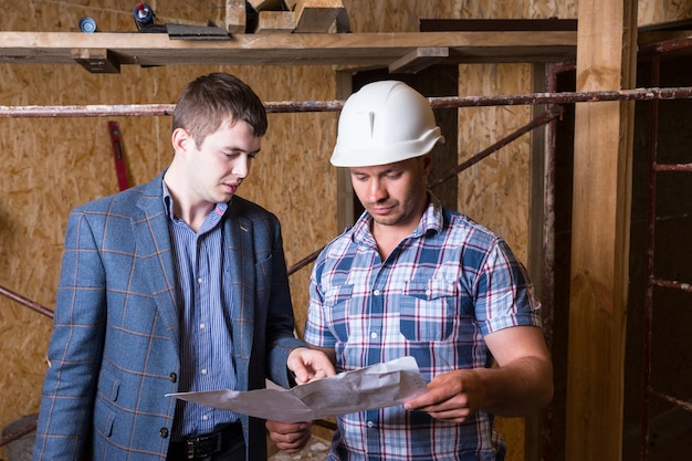 Architekt und Bauarbeiter Vorarbeiter prüfen gemeinsam Pläne im unfertigen Gebäude