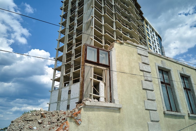 Architektonisches Detail des hohen Rahmens des im Bau befindlichen monolithischen Betongebäudes und des alten abgerissenen Hauses vor der Immobilienentwicklung