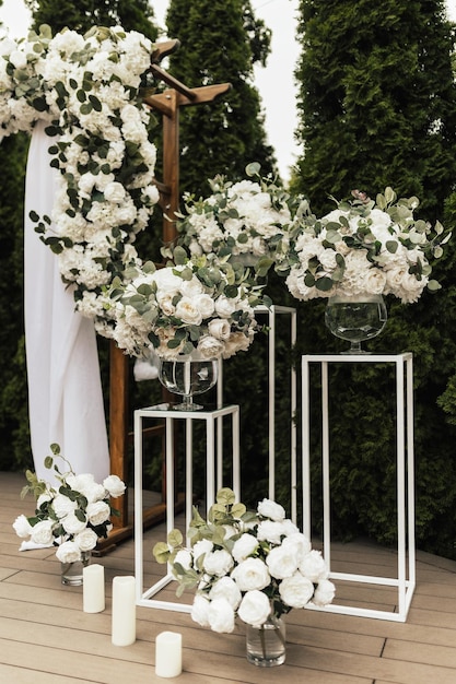 Un arco de boda blanco con flores blancas y vegetación.