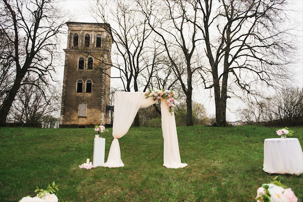 Arco de boda decorado con tela y flores al aire libre. Hermosa boda organizada. Ceremonia de boda en césped verde en el jardín. Parte de la decoración festiva, arreglo floral.