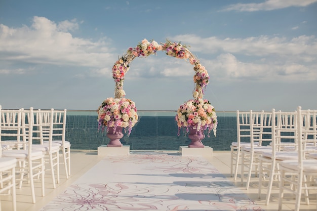 Arco de boda con flores frescas sobre un fondo de mar. Jarrones con flores frescas.