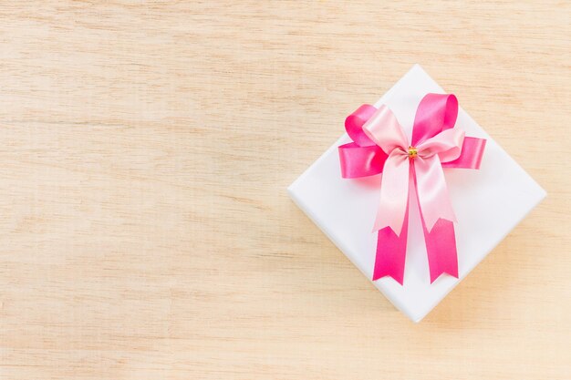 Arco de cinta rosa y caja de regalo blanca sobre fondo de madera