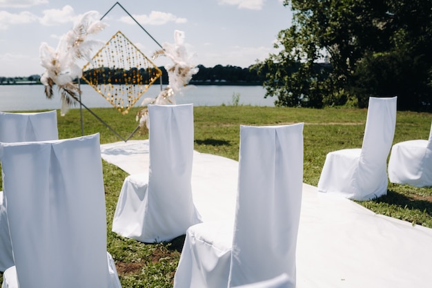 Arco de casamento decorado na natureza. cerimônia de casamento com um arco decorado com penas de estilo retrô em um fundo de lago