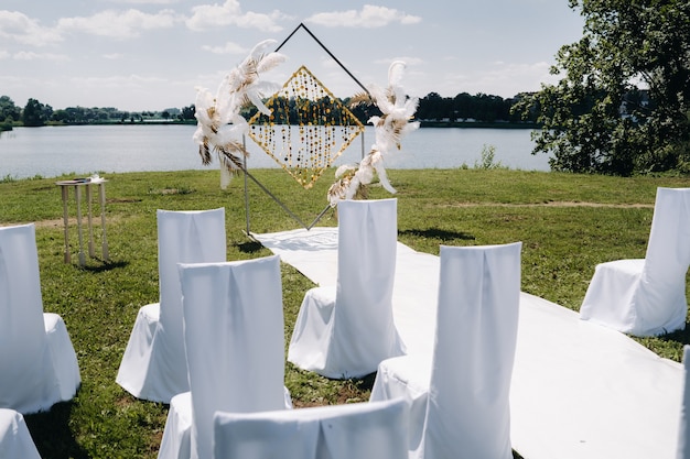 Foto arco de casamento decorado na natureza. cerimônia de casamento com um arco decorado com penas de estilo retrô em um fundo de lago