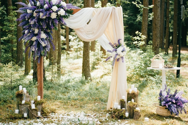 Arco de casamento lindo com flores azuis e elementos decorativos em pé na floresta. Cenário de casamento em estilo rústico