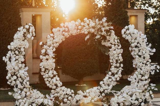 Arco de casamento redondo com flores brancas e vegetação ao pôr do sol