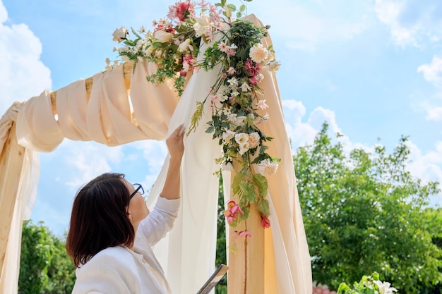 Arco de decoração com têxteis com flores e plantas Proprietário organizador de mulher com tablet digital perto do arco de casamento