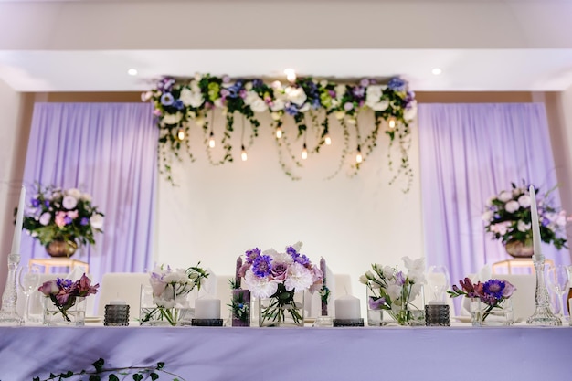 Arco de mesa festivo fica decorado com composição de flores rosa roxas violetas e velas verdes no salão de banquetes Recém-casados de mesa na área de banquete na festa de casamento