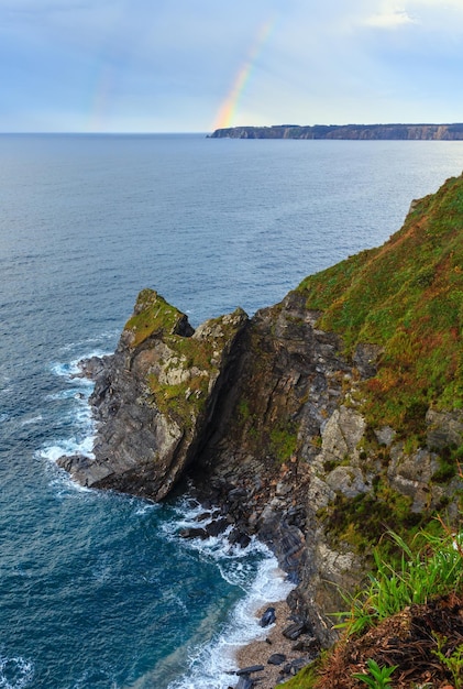 Arco iris de colores sobre la orilla del mar. Paisaje rocoso de la costa de la noche de verano del océano Atlántico (cerca de Luarca, Asturias, la bahía de Vizcaya, España).