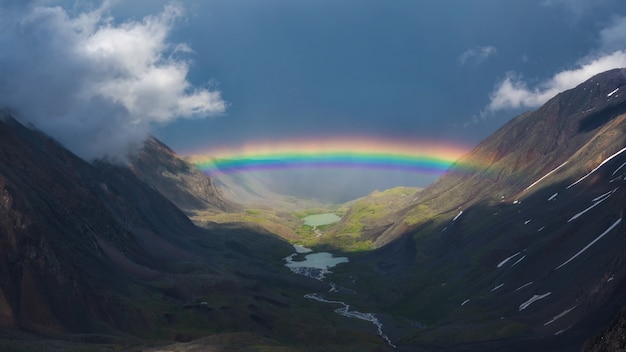 Arco iris completo sobre un valle de montaña. Paisaje alpino atmosférico con montañas nevadas con arco iris en tiempo lluvioso y soleado.