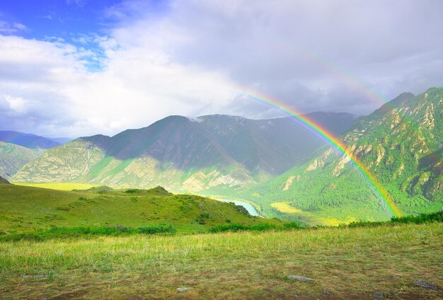 Arco-íris em um vale de montanha Encostas verdes entre montanhas rochosas sob um céu azul nublado Altai