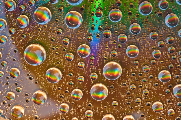 El arco iris estalla dentro de gotas de agua sobre una superficie metálica reflectante