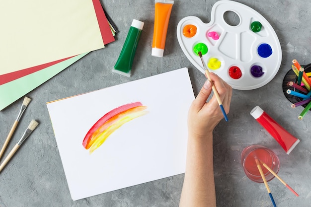 Arco iris de pintura de mano de mujer en cuaderno de bocetos con pincel de dolor con materiales de arte alrededor