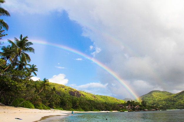 Arco iris sobre isla tropical y playa blanca en Seychelles